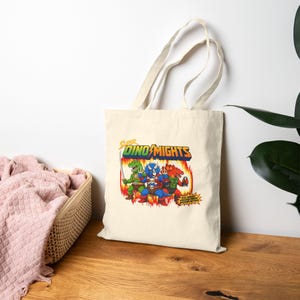 Super DinoMights Tote Bag  Retro Cartoon Parody Canvas Tote | 80s Style Dinosaur Graphic Bag | Vintage Aesthetic Streetwear Tote