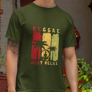 Puede incluir: Camiseta verde oliva con un diseño temático de reggae. El diseño presenta la palabra "Reggae" en rayas verticales rojas, amarillas y verdes, junto con palmeras y el texto "Just Relax". La persona lleva pantalones blancos.