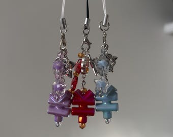 Peut inclure: Trois breloques perlées violettes, rouges et bleues, chacune avec un design unique. Les breloques sont suspendues à des fermoirs en métal argenté et à des cordons blancs. Les perles sont de formes et de tailles variées.