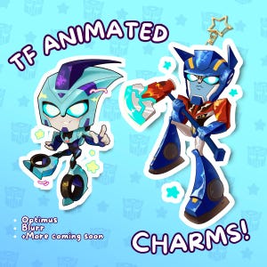 Puede incluir: Dos colgantes de personajes de dibujos animados, uno azul claro y otro azul y rojo, con el texto "TF ANIMATED CHARMS!" y los nombres de los personajes. El personaje azul claro es Blurr, y el personaje azul y rojo es Optimus. El fondo es azul claro con patrones de estrellas y logotipos.