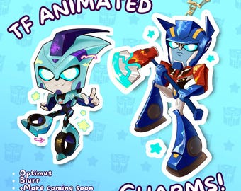 Könnte beinhalten: Zwei Cartoon-Charakter-Anhänger, einer hellblau und einer blau und rot, mit dem Text "TF ANIMATED CHARMS!" und den Namen der Charaktere. Der hellblaue Charakter ist Blurr, und der blau-rote Charakter ist Optimus. Der Hintergrund ist hellblau mit Stern- und Logomustern.