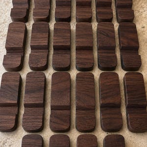 Puede incluir: Una colecci&oacute;n de veinti&uacute;n soportes de tel&eacute;fono de madera marr&oacute;n oscuro. Cada soporte es rectangular con una base curva y una ranura para sostener un tel&eacute;fono. La veta de la madera es visible en cada soporte.