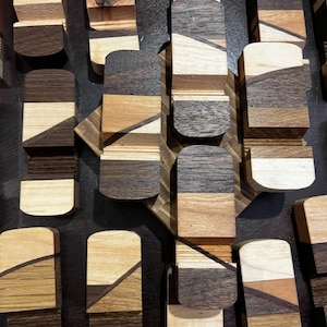 Puede incluir: Vista a&eacute;rea de m&uacute;ltiples objetos de madera con tapas redondeadas. Los objetos est&aacute;n hechos de varios tipos de madera, mostrando una gama de colores que va del beige claro al marr&oacute;n oscuro. Cada pieza est&aacute; compuesta por secciones de madera en capas, creando un efecto rayado.