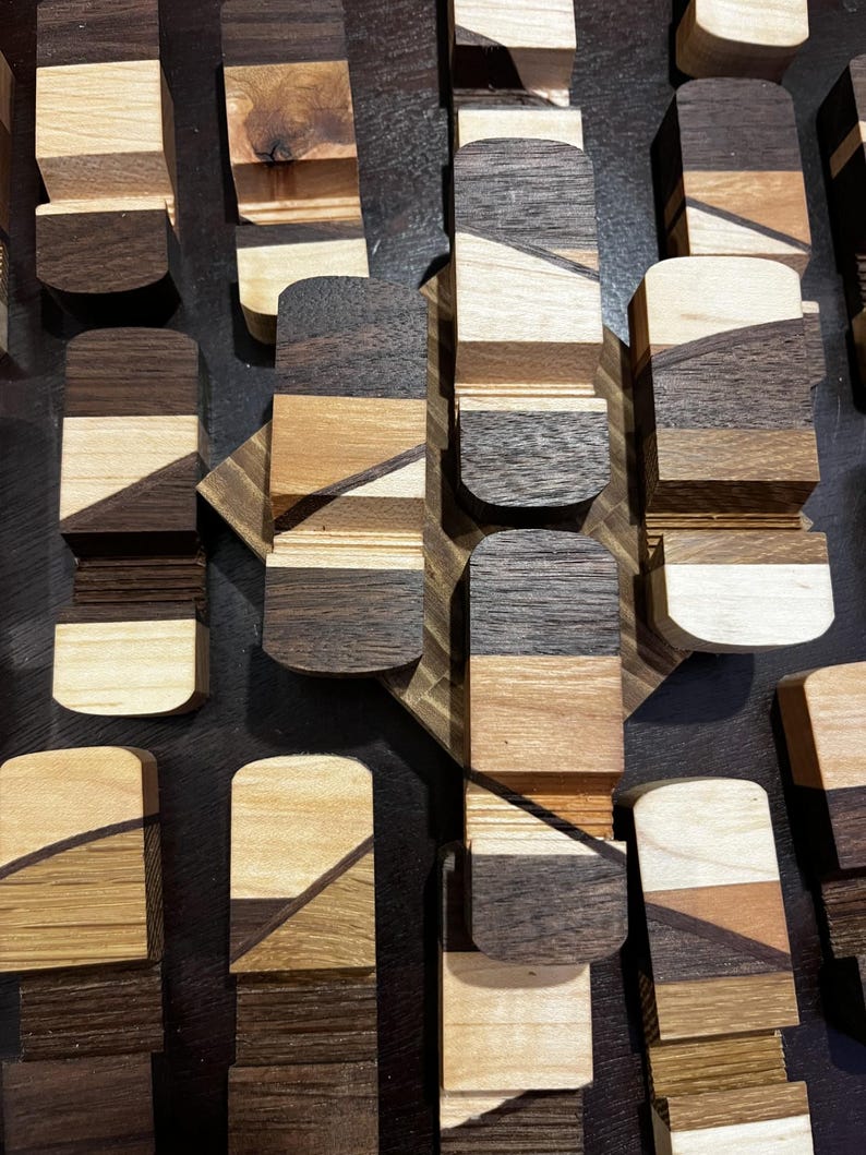 Puede incluir: Vista a&eacute;rea de m&uacute;ltiples objetos de madera con tapas redondeadas. Los objetos est&aacute;n hechos de varios tipos de madera, mostrando una gama de colores que va del beige claro al marr&oacute;n oscuro. Cada pieza est&aacute; compuesta por secciones de madera en capas, creando un efecto rayado.
