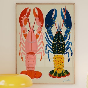 Może przedstawiać: Oprawiony wydruk z ilustracjami dwóch kolorowych homarów, różowego i niebieskiego, wisi nad białą szafką. Żółta lampa w kształcie grzyba, pasiasty kubek i niebieska miska z cytrynami stoją na szafce.