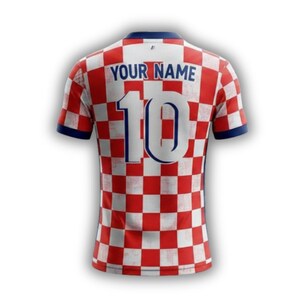May include: A red and white checkered soccer jersey with the number 10 and the text "YOUR NAME" in blue. The jersey has blue trim on the collar and sleeves. The jersey is a sports apparel item.