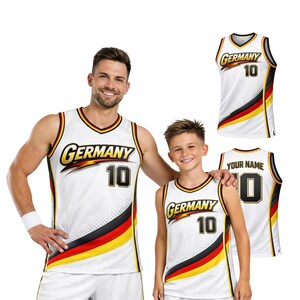 May include: White basketball jerseys with the word "Germany" in gold script and the number "10" in black. The jerseys feature a black, red, and yellow stripe design. One jersey has "Your Name" on the back.