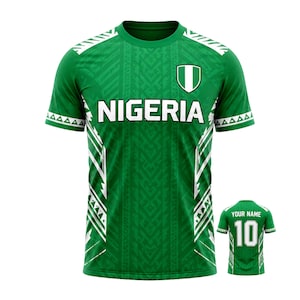 May include: Green Nigeria football shirt with white detailing and the word "NIGERIA" across the chest. The shirt has a shield emblem and a geometric pattern. A smaller image shows the back with "YOUR NAME" and the number "10".