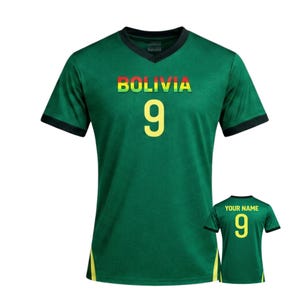 Puede incluir: Camiseta de fútbol verde de Bolivia con cuello en V y mangas cortas. La palabra "BOLIVIA" está impresa en el pecho en amarillo, rojo y verde. El número "9" está impreso en amarillo debajo. Una versión más pequeña de la camiseta se muestra abajo a la derecha.