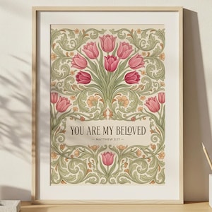 May include: Framed art print featuring a floral design with pink tulips and green foliage. The text "YOU ARE MY BELOVED - MATTHEW 3:17" is displayed on a banner. The print is in a wooden frame and rests on a wooden desk.