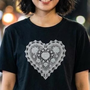 May include: Black t-shirt with a white, lace-style heart motif. The heart is centrally placed and has detailed patterns. The shirt has short sleeves and a round neck.