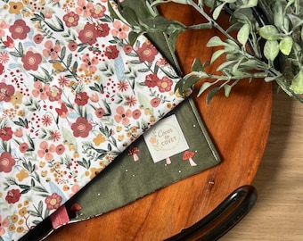 May include: Two floral patterned bandanas, one white with red and pink flowers, the other green with mushroom graphics. The bandanas are on a wooden tray with a black rim, and greenery.