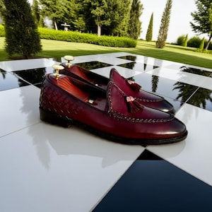 May include: A pair of burgundy leather loafers with woven detailing on the vamp and decorative tassels. The shoes have a classic design with a polished finish, suitable for formal or semi-formal occasions.