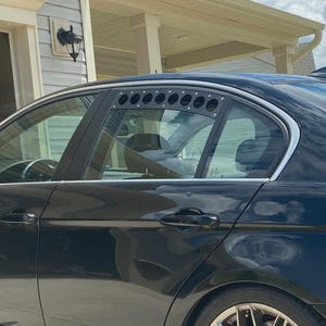 May include: Black sedan with custom wheels parked in a driveway. The car has tinted windows and a sunroof. The background includes a garage, a house, and a blue sky with clouds.