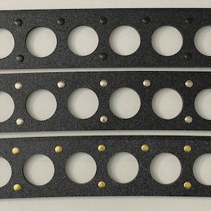 May include: Three black rectangular gaskets with large circular holes and smaller fastener holes. The top gasket has black fasteners, the middle one has silver fasteners, and the bottom one has gold fasteners. Automotive parts.