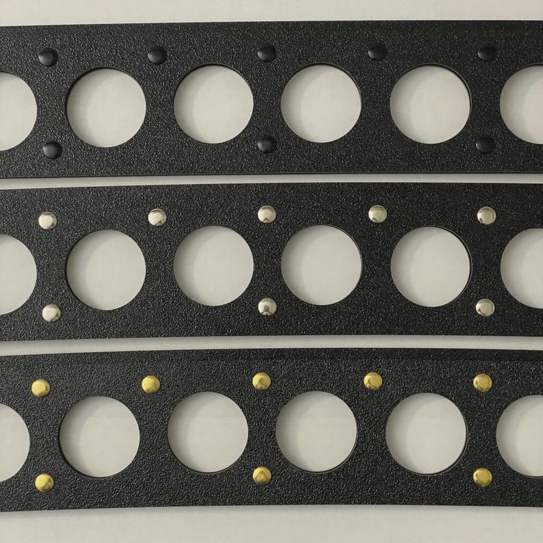 May include: Three black rectangular gaskets with large circular holes and smaller fastener holes. The top gasket has black fasteners, the middle one has silver fasteners, and the bottom one has gold fasteners. Automotive parts.