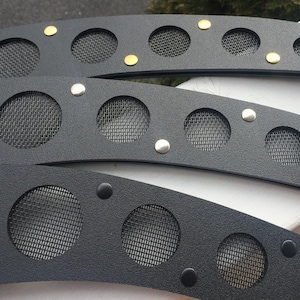 May include: Close-up of three black metal decorative pieces. Each piece has circular mesh inserts and is adorned with silver and gold-colored rivets. The pieces have a curved shape and a textured surface.