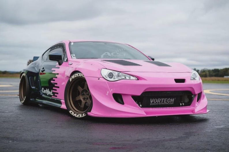 May include: A modified pink sports car with black detailing and a body kit. The car has custom wheels, a front splitter, and the word "Vortech" on the front. The car has the word "Certified" on the side.