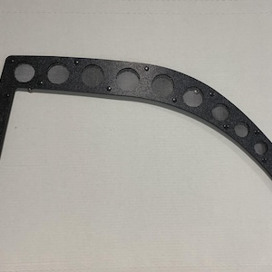 May include: Black curved metal bracket with multiple circular mesh inserts. The bracket has a right-angle extension and is secured with small rivets. The design suggests a functional or decorative automotive or industrial component.