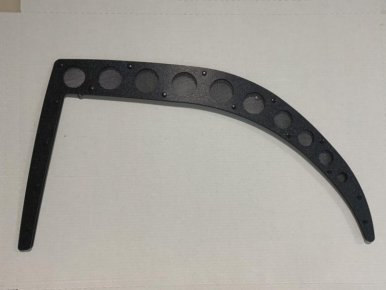 May include: Black curved metal bracket with multiple circular mesh inserts. The bracket has a right-angle extension and is secured with small rivets. The design suggests a functional or decorative automotive or industrial component.