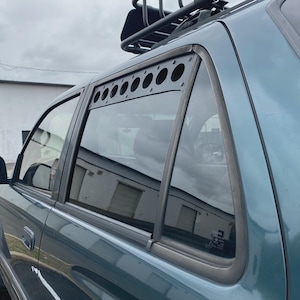 May include: A teal green SUV with a black roof rack and a black metal window mesh screen. The mesh screen is installed on the rear passenger side window.