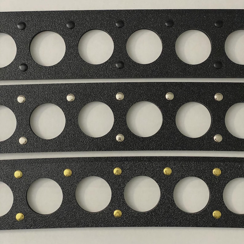 May include: Three black rectangular gaskets with large circular holes and smaller fastener holes. The top gasket has black fasteners, the middle one has silver fasteners, and the bottom one has gold fasteners. Automotive parts.