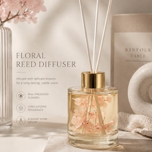 May include: A clear glass reed diffuser bottle with a gold-toned cap, containing light pink preserved flowers submerged in liquid. Three white reed sticks extend from the top. Text on the image reads: Floral Reed Diffuser, Infused with delicate blooms for a long-lasting, subtle scent, Real Preserved Flowers, Long-lasting Fragrance, Elegant Home Décor.