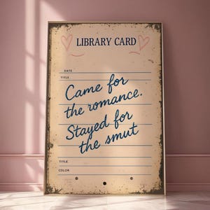 May include: A framed vintage-style library card print with the text "Came for the romance. Stayed for the smut" in blue script. The print has a distressed, aged appearance with hearts and lines.