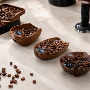 Könnte beinhalten: Holzlöffel für Kaffeebohnen mit integrierten Digitalwaagen. Die Löffel sind mit gerösteten Kaffeebohnen gefüllt, und die Waagen zeigen Gewichte wie 128 Gramm und 127 Gramm an. Die Löffel sind aus dunklem Holz gefertigt.