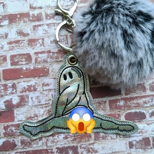 May include: A silver iridescent ghost-shaped keychain with a surprised face and a fluffy white and black pom-pom.