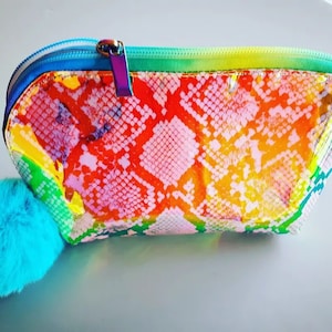 May include: A rainbow iridescent cosmetic bag with a faux fur pom-pom zipper pull. The bag has a snakeskin pattern.