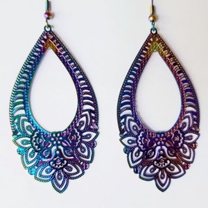 May include: A pair of iridescent teardrop-shaped earrings with a detailed cutout design. The earrings are made of metal and have a rainbow finish.