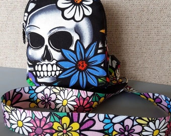 May include: A black and white skull with colorful flowers printed on a small bag with a matching colorful floral strap.