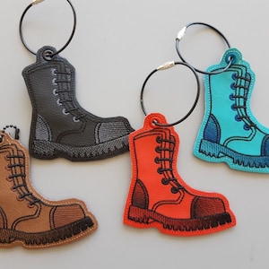 May include: Four embroidered boot keychains in different colors: black, brown, orange, and blue. Each keychain has a black metal ring.