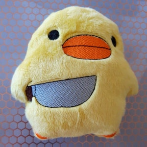 May include: A yellow plush toy shaped like a duck with a knife in its mouth. The duck has a black eye, an orange beak, and a gray knife.