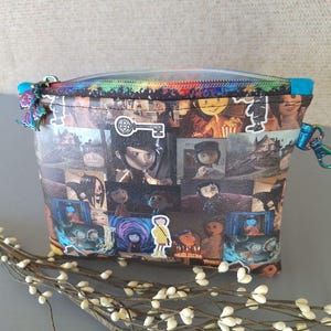 May include: A colorful zippered pouch with a collage of images from the movie "Coraline" printed on the front. The images include the main character, Coraline, and other characters from the film.