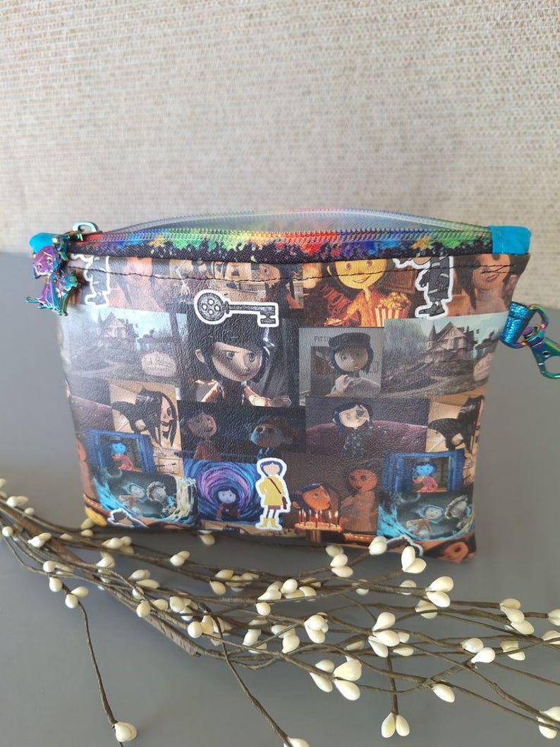 May include: A colorful zippered pouch with a collage of images from the movie "Coraline" printed on the front. The images include the main character, Coraline, and other characters from the film.