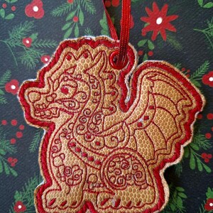 May include: A red and brown embroidered Christmas ornament shaped like a dragon with intricate details. The ornament has a loop at the top for hanging.