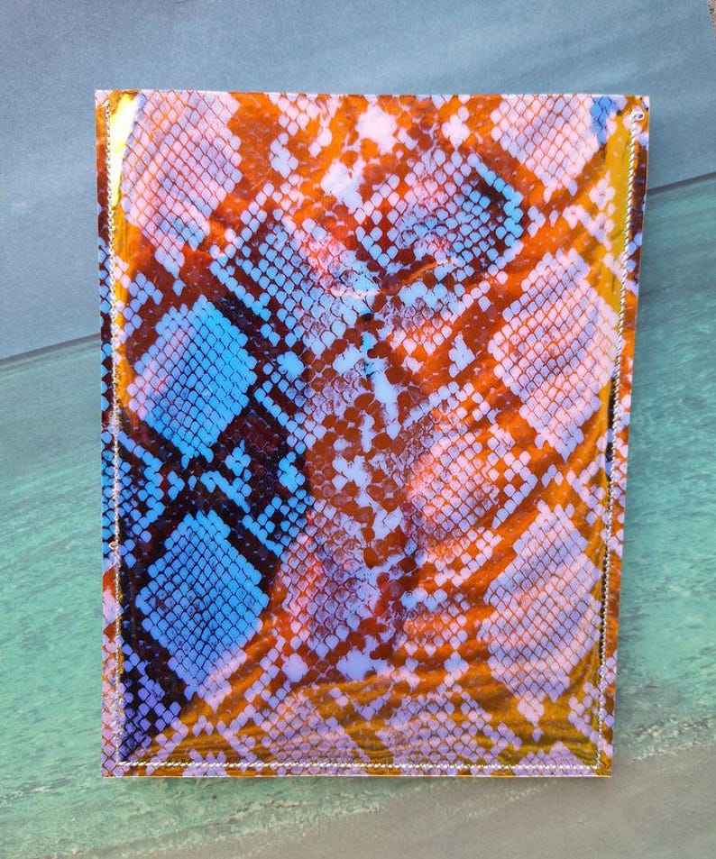 Peut inclure: Un portefeuille rectangulaire avec un motif peau de serpent dans les tons orange, bleu et blanc. Le portefeuille a une finition brillante et est cousu sur les bords. Le motif imite les &eacute;cailles d'un serpent.