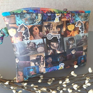 May include: A black and white patterned zippered pouch with a variety of images from the movie "Coraline". The pouch has a silver zipper and a silver key charm.