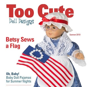 Puede incluir: Una muñeca con un gorro blanco con una cinta roja, un cuello de encaje blanco y un vestido estampado en azul y blanco, sosteniendo una pequeña bandera estadounidense. La muñeca aparece en la portada de una revista titulada "Too Cute Doll Designs" con el texto "Betsy Sews a Flag" y "Summer 2019".