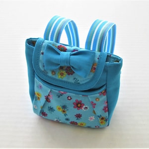 May include: A small blue backpack with a floral print and a blue bow. The backpack has two adjustable straps.