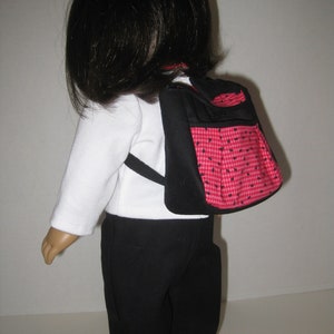 May include: A doll wearing a white shirt, black pants, and a red and black checkered backpack.