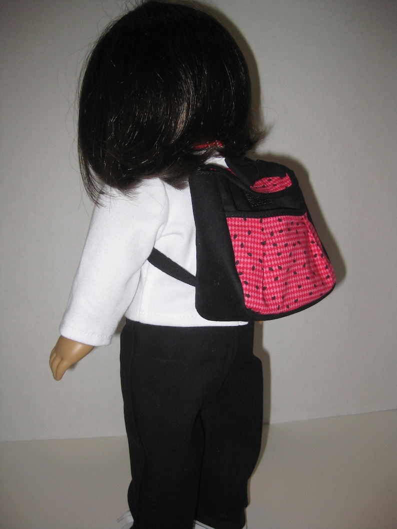 May include: A doll wearing a white shirt, black pants, and a red and black checkered backpack.