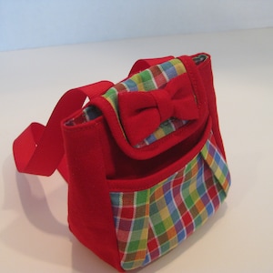 May include: A small red and multi-colored plaid backpack with a red bow on the front.