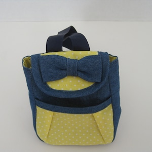 May include: A small blue denim backpack with a yellow polka dot lining and a blue denim bow on the front.