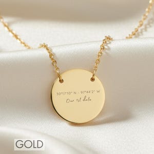May include: A gold-toned circular pendant necklace featuring an engraved coordinate set reading 30°17'10" N - 97°44'2" W and the text Our 1st date. The pendant is suspended from a delicate matching gold-toned chain with a polished, reflective finish.