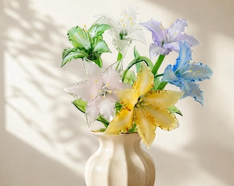 May include: A bouquet of multi-colored glass flowers in a cream-colored ceramic vase. The flowers feature translucent petals in shades of white, green, light purple, blue, pale pink, and yellow, each with delicate green stems and yellow centers.