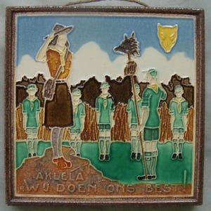 May include: A framed ceramic tile with a scout theme. The artwork shows a group of scouts and a leader in a field, with text at the bottom. The color palette includes shades of brown, green, blue, and yellow.