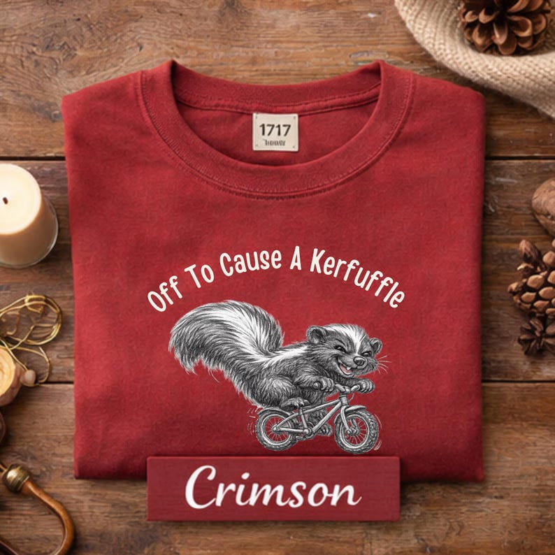 May include: Crimson-colored sweatshirt with the text "Off To Cause A Kerfuffle" and a skunk riding a bicycle. The sweatshirt has a crew neck and a small tag that reads "1717".